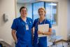 Two healthcare professionals in blue scrubs standing together
